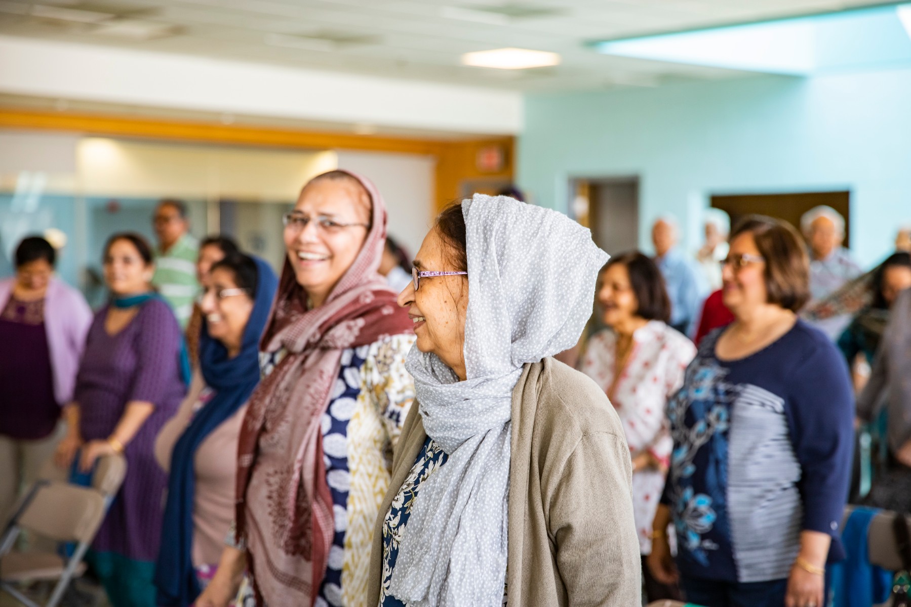 A photo of women standing in a room full of other women talking and laughing.