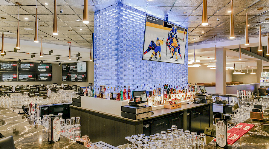 A square bar in the middle of a room with a large TV hung on the centre wall.