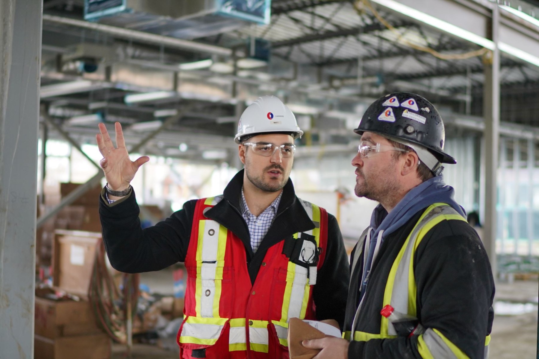 A photo of two Chandos construction workers in safety gear on site discussing a project.