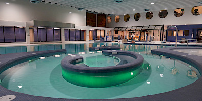 A photo of a lazy river in an aquatic centre with green lighting in the centre of the lazy river and black tile surrounding it.