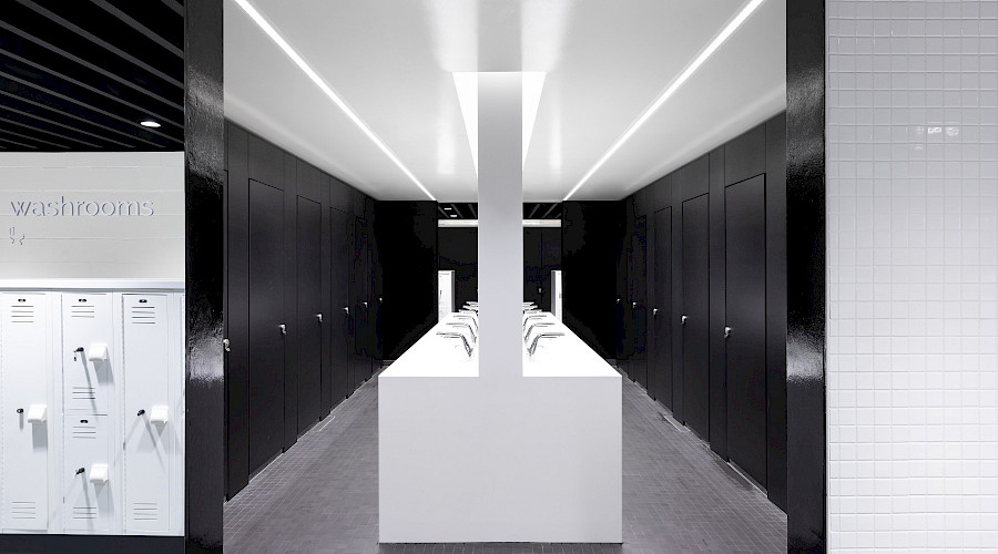 A large white island with multiple sinks centered between rows of black bathroom stalls.