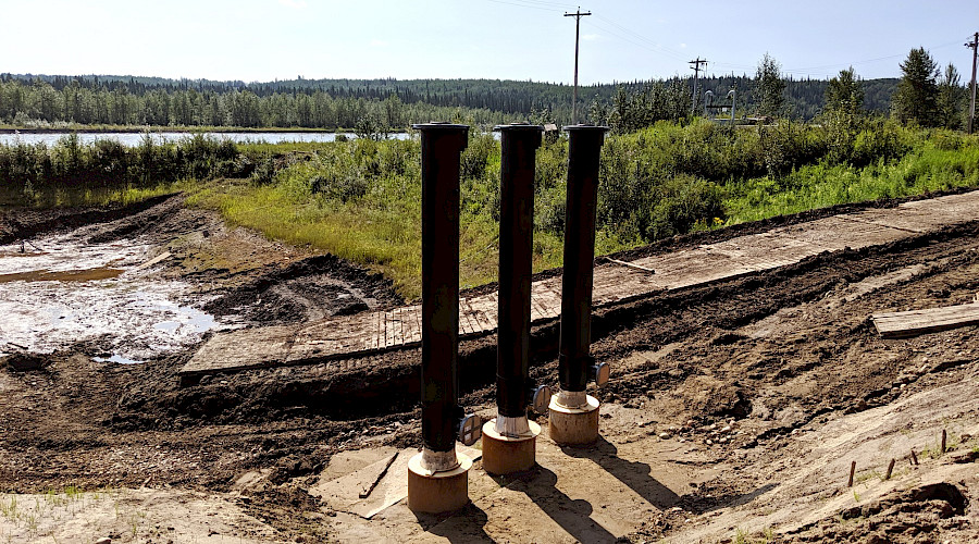 Pipes in the ground on a construction site with a river and trees in the background.