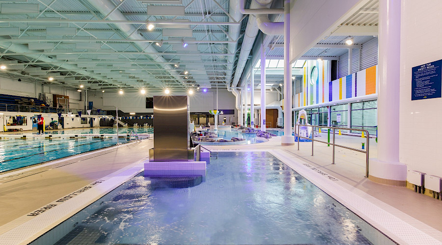 A hot tub in front of a lazy river beside a large pool with multiple lanes.