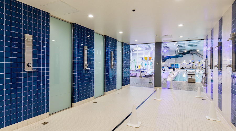 Open showers on blue tiled walls in front of a large pool.