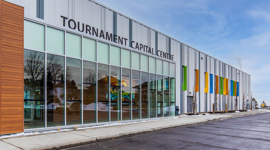 The exterior of the Canada Games Aquatic Centre with signage above large windows that reads 