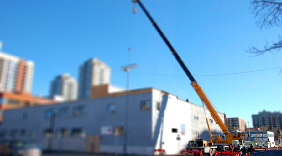 A large crane in focus in front beside a large, blurred building.