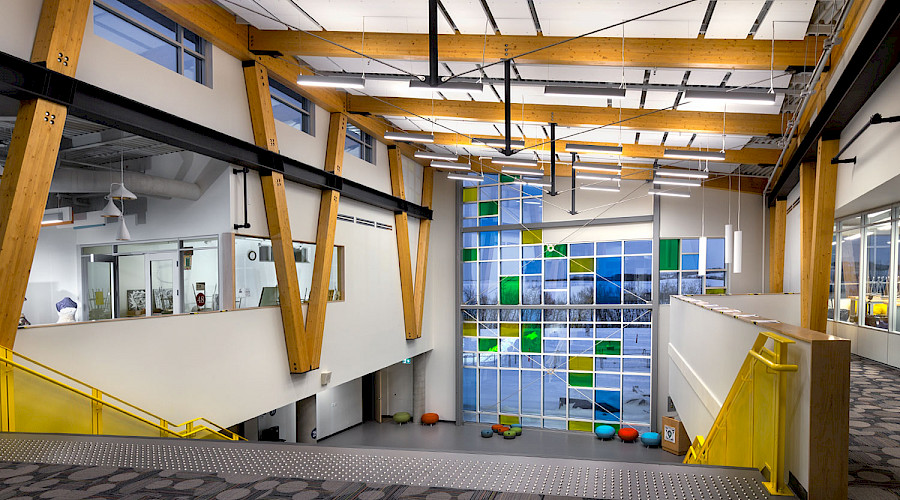 The view from the top of a large staircase, looking onto large multicoloured windows and wooden beams on the ceiling.