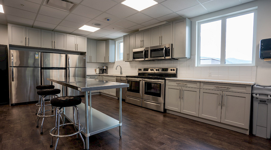A kitchen with white cupboards, stainless steel appliances, and a three stools at a stainless steel island.