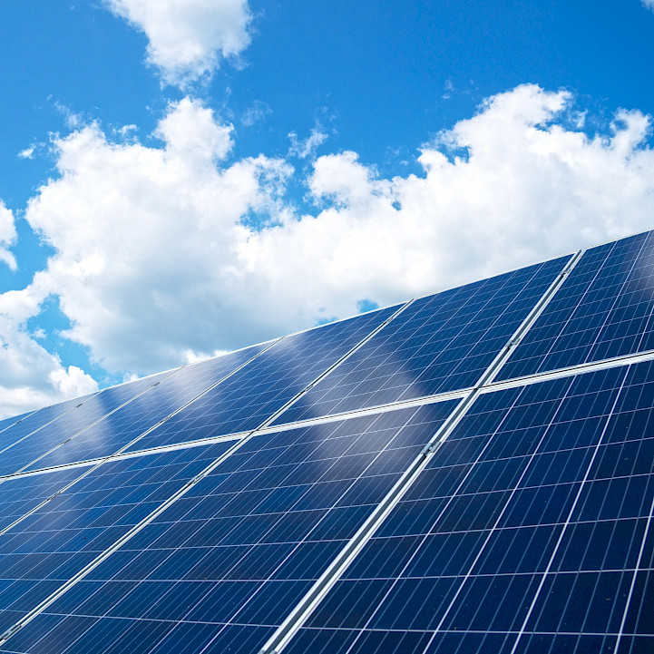 A photo of solar panels with a cloudy, blue sky in the background.