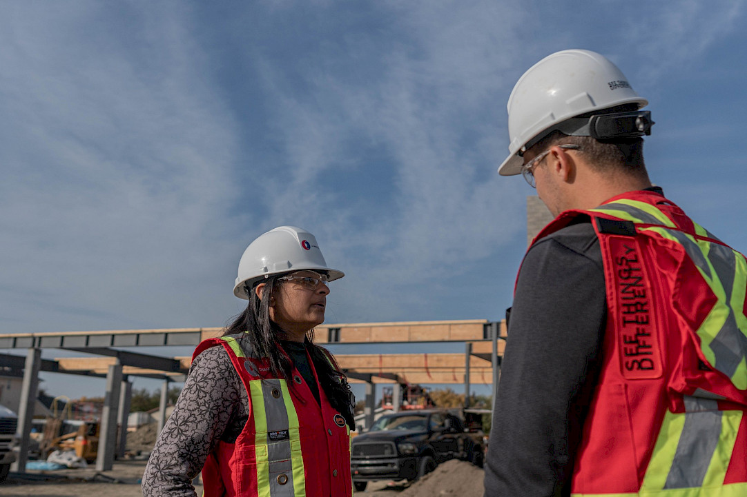 A female Chandos construction worker discussing a project on site with another Chandos construction worker wearing a vest that reads 
