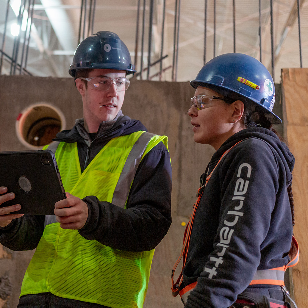 Two Chandos construction workers reviewing plans and using surveying equipment