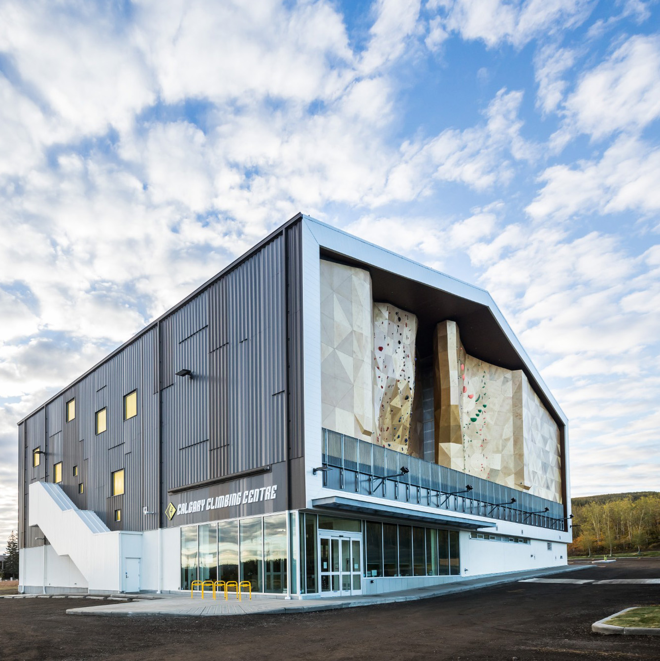 A photo of the Calgary Climbing Centre from the outside, featuring it's large climbing wall with a cloudy blue sky in the background.