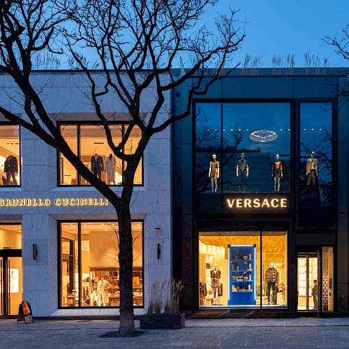 A photo of two retail stores lit up inside on Yorkville Avenue in Toronto, Ontario, with white stone and sleek black exteriors.