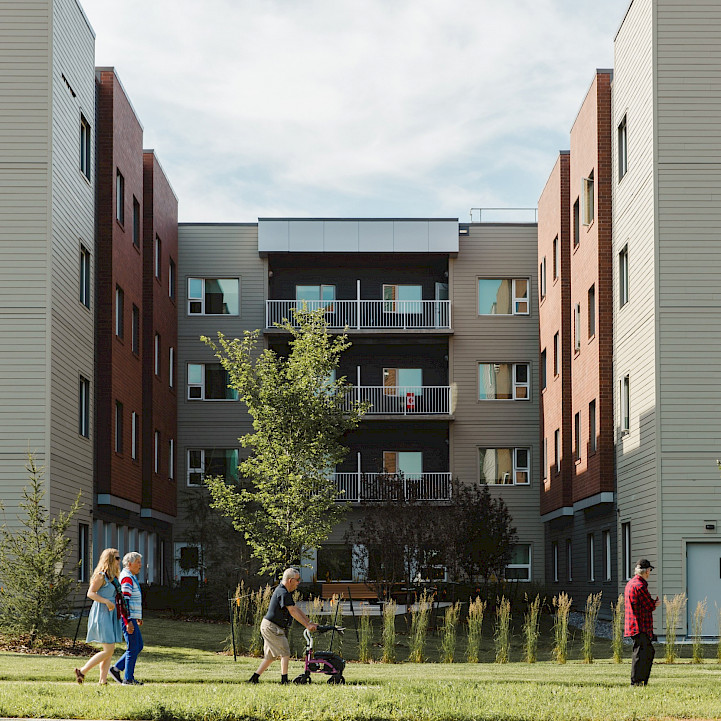 People walking outside the Sakaw Terrace Senior Housing facility on a sunny day.