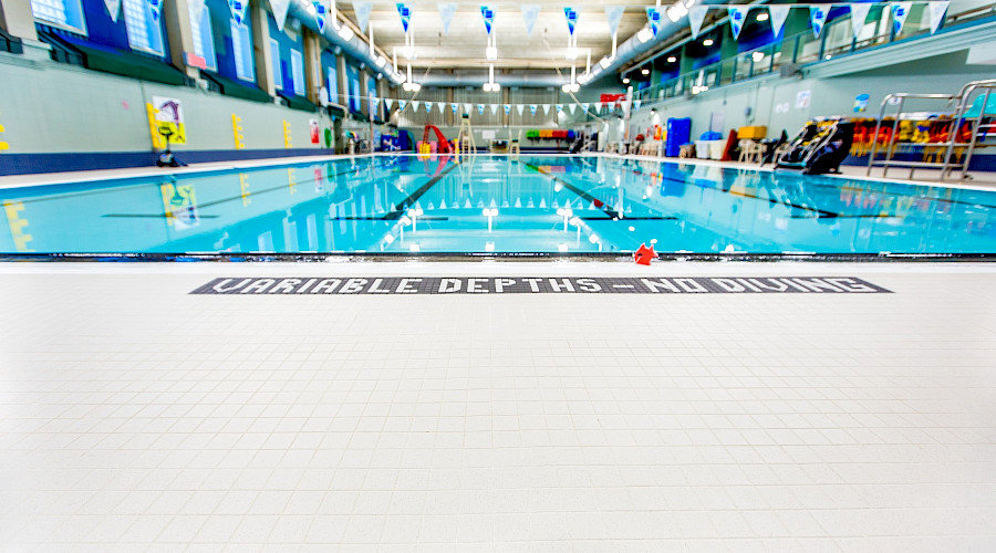Tile in front of a bright blue pool with multiple lanes.