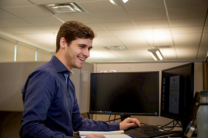 A Chandos construction worker standing at his desk, smiling as he works on his computer.