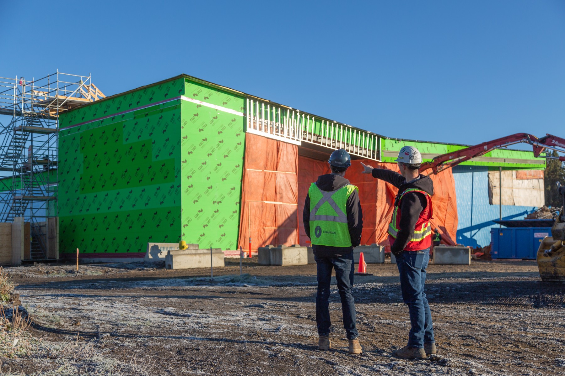 Two Chandos construction workers in safety gear on a project site, talking about a project.