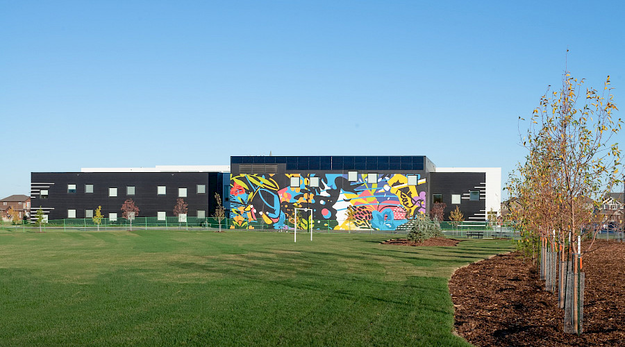 A field of green grass in front of the exterior of Garth Worthington school, with it's colourful exterior mural on display.