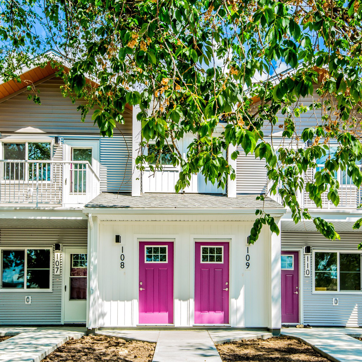 A duplex with two hot pink doors behind multiple tree branches with green leaves.
