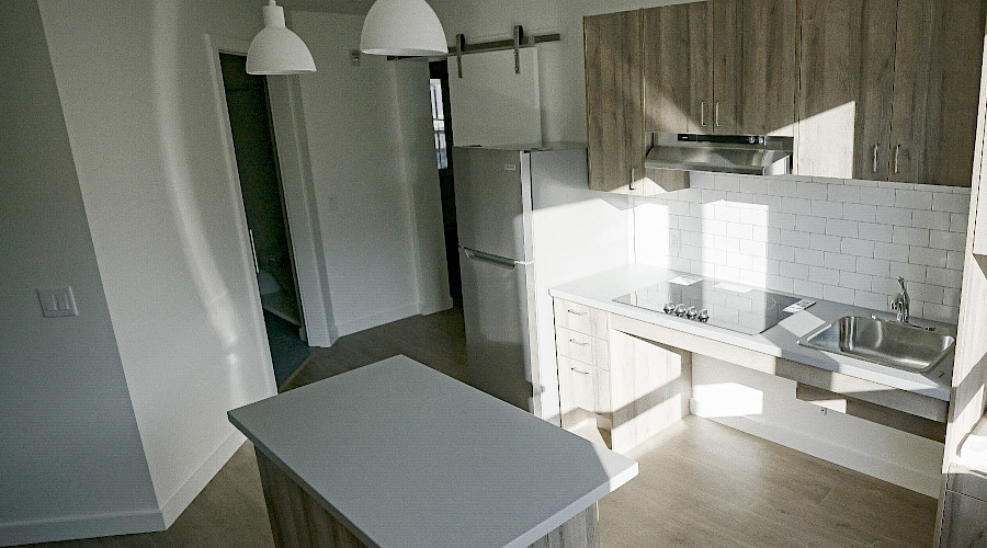 An island in a kitchen with light wood cupboards, white countertops and backsplash, with doors leading to other rooms visible in the background.