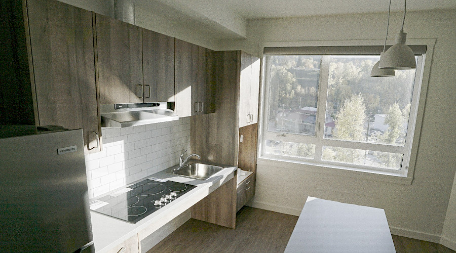 A kitchen with light wood cupboards, white walls and countertops, and a large window.