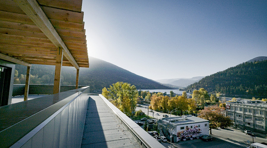 A photo taken from the roof of a building, looking onto a street lined with orange and green trees with a lake and hills in the background.