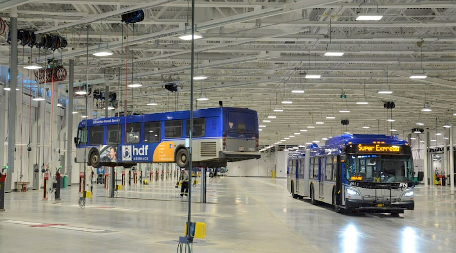 A city bus next to another city bus lifted to be worked on in a maintenance garage.