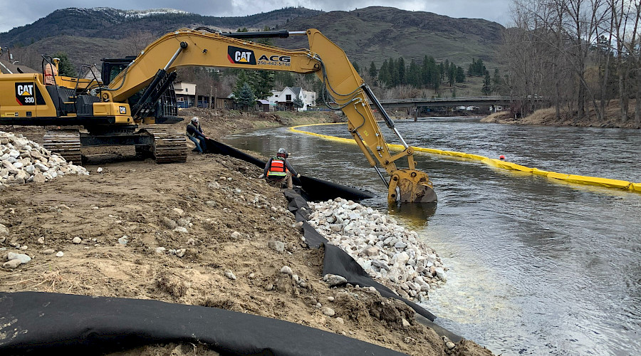 Construction workers using an excavator alongside a river.