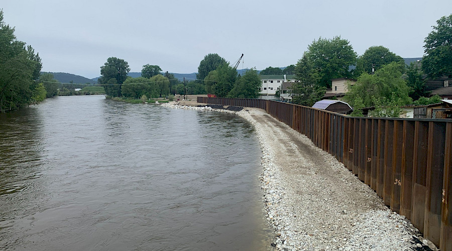 A fence on a rocky river shore in front of rows of houses.