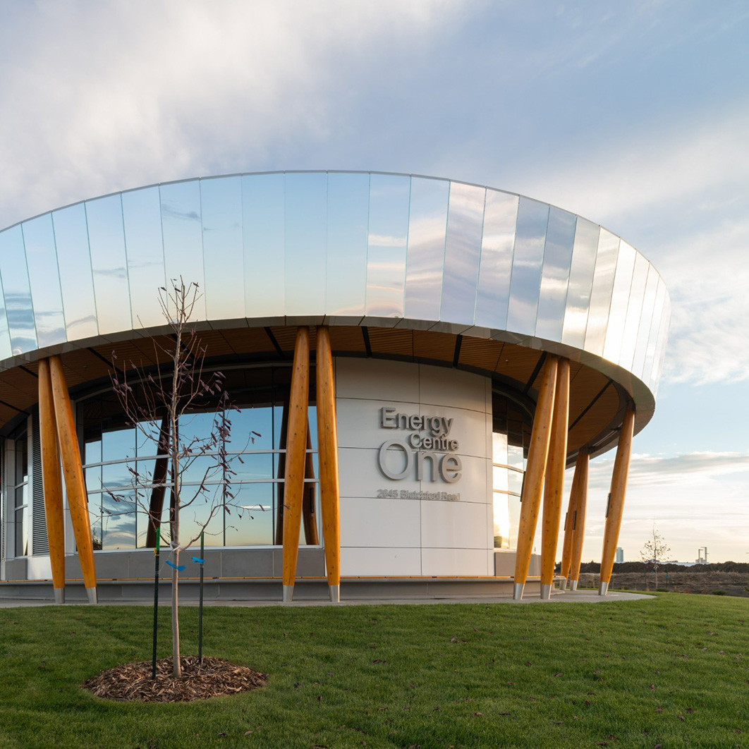 A photo of a rounded corner of the Blatchford energy centre building with a mirrored building envelope against a blue sky with clouds