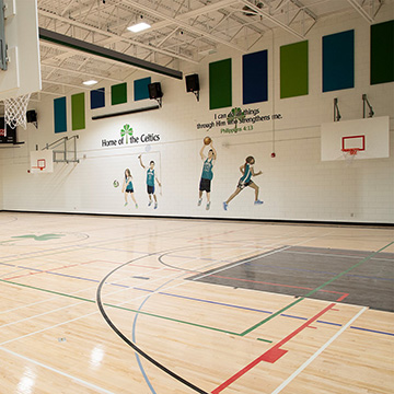 An elementary school's gymnasium with artwork depicting children playing sports on the walls.