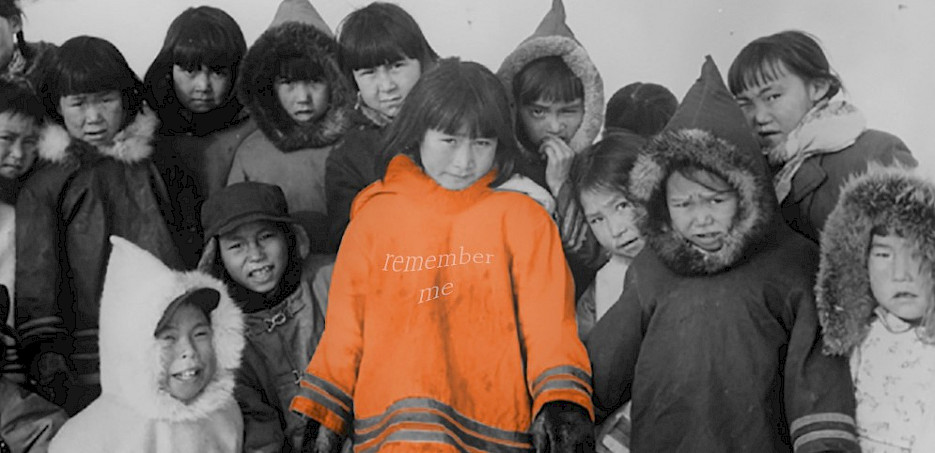 A black and white photo of a group of Indigenous children with one girl in the middle wearing a bright orange shirt that says "Remember me?".