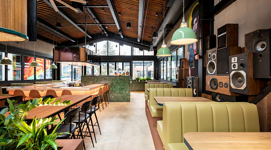 Rows of tables and booths along a wall lined with stereos in a large restaurant with wood ceilings. At the The Central Taps and 33 Acres restaurant and 33 Acres Brewing bar in downtown Calgary