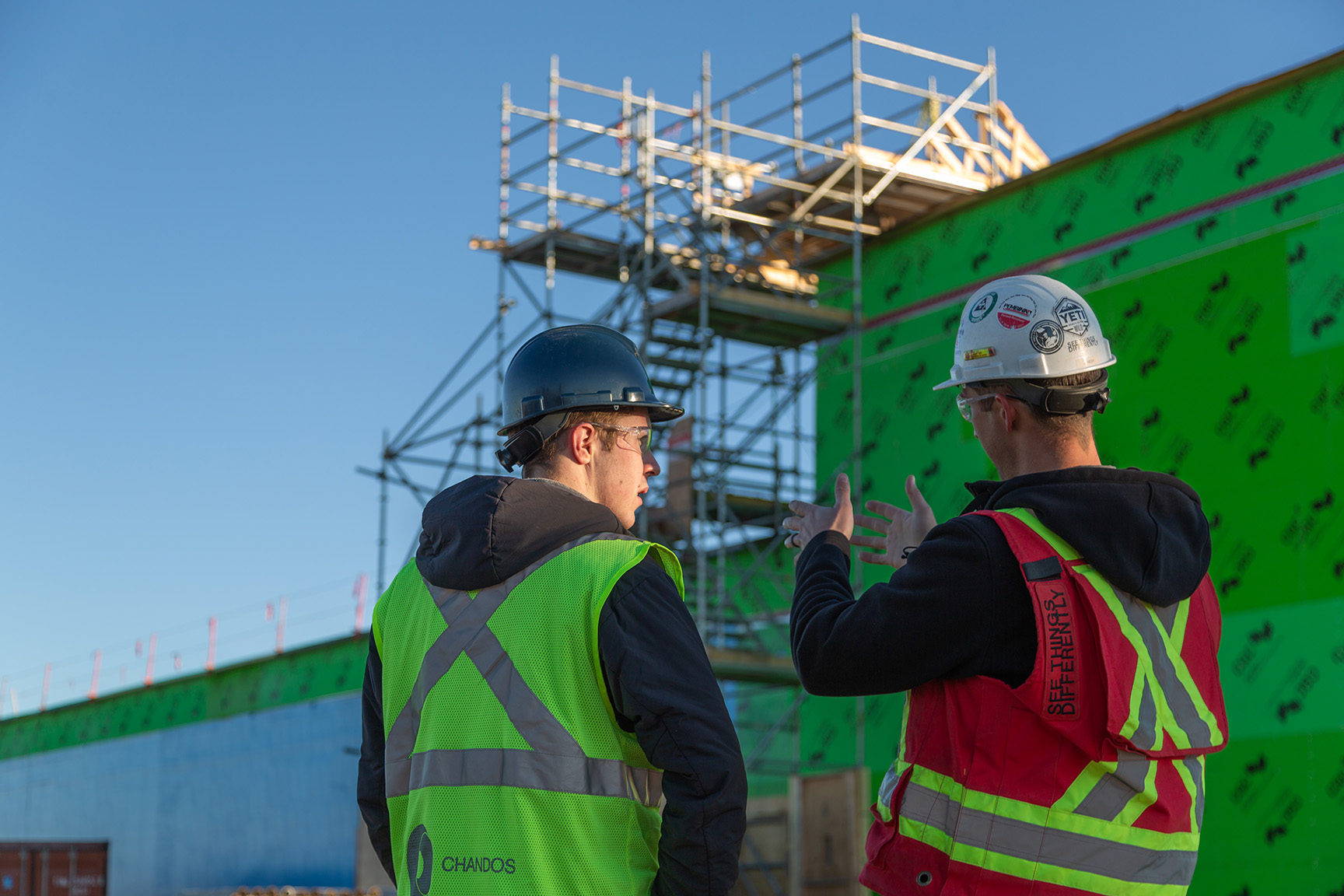 Two Chandos construction workers wearing safety gear discussing a project on site.