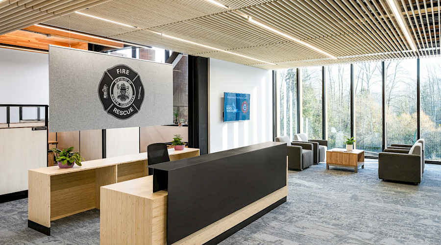 Interior shot of the new Maplewood Fire and Rescue Centre, featuring the waiting room and lobby with floor to ceiling windows and wood paneling. Built by Chandos Construction Vancouver