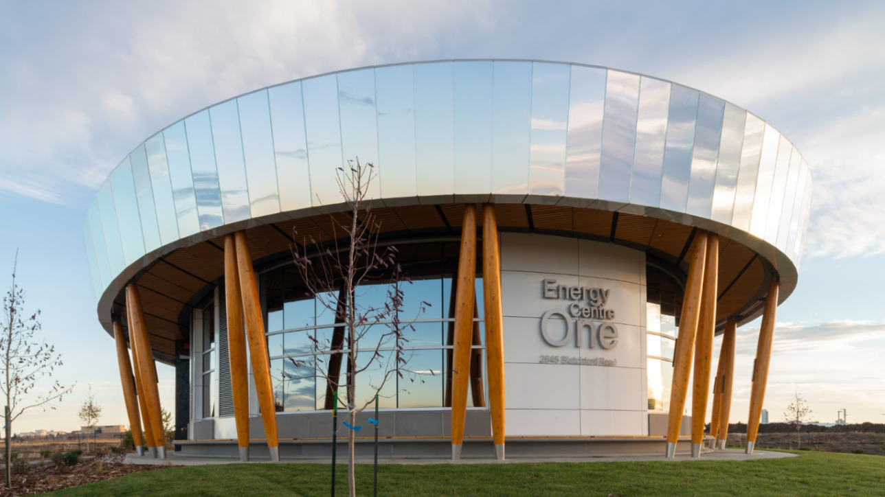 A photo of the Blatchford Energy Centre in Edmonton, with it's mirrored exterior reflecting a cloudy blue sky.