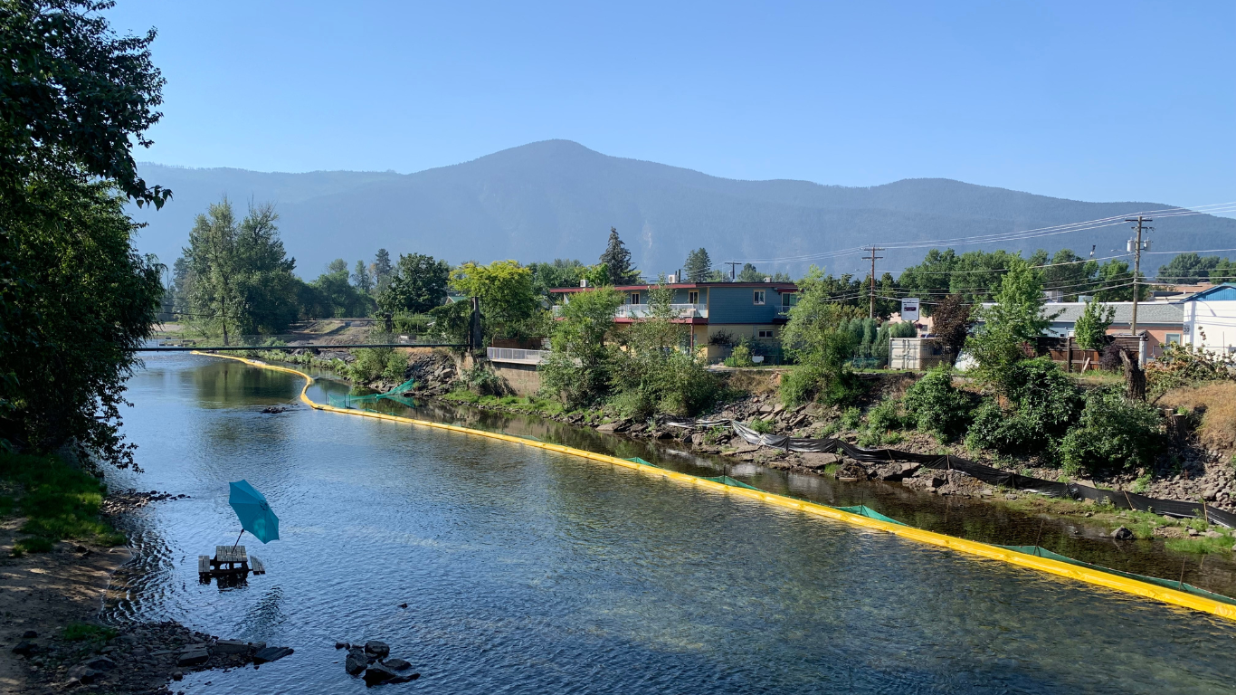 A river beside trees and houses, with large hills in the background.