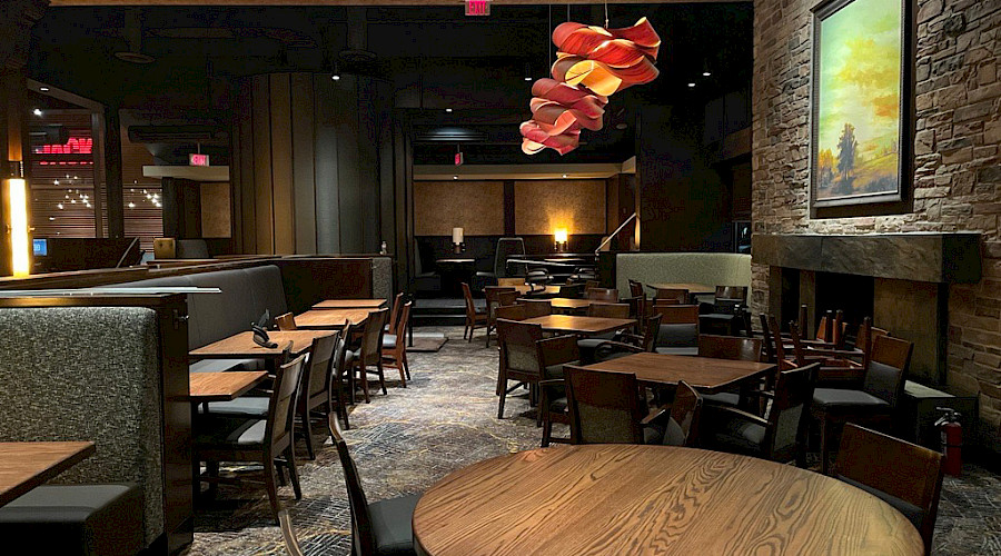 interior shot of the Keg dining room, refurbished by Chandos Construction. The new reupholstered booths are dark grey and adjacent to the dining tables, fireplace, and artwork.