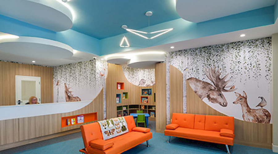 Image of the Child and Family Centre front lobby built by Chandos Construction Calgary. The room is a peaceful blue with cloud shaped lighting and orange couches.