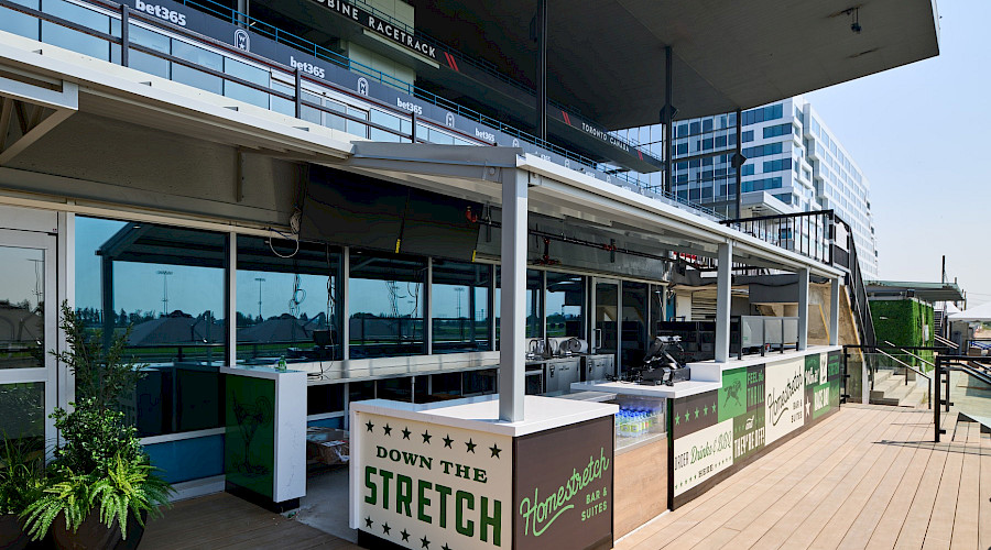 Image of the outdoor kitchen built by Chandos Construction Toronto at the Woodbine Apron Patio. The wooden flooring is complimented by the green accents on the bar siding.