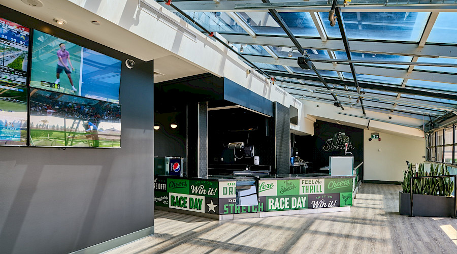 Interior shot of the new bar built by Chandos Construction Toronto at the Woodbine Apron Patio. The kick guard at the bar is decorated with bright green lettering that spells out phrases like 