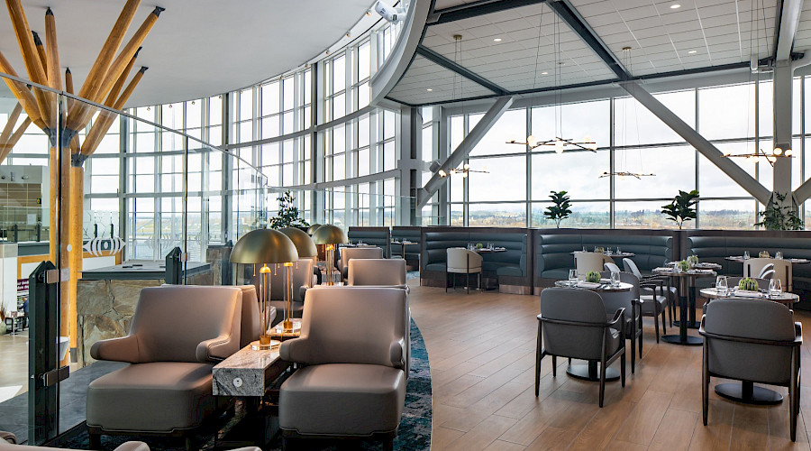 Interior image of the new Plaza Premium Lounge in YVR built by Chandos Construction Vancouver. Image showcases the lounge section with comfortable chairs, and floor to ceiling windows that lead to the airport runways.